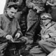 Ernie Pyle sits on the ground in a group of soldiers talking.