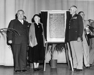 Three people stand next to an Ernie Pyle remembrance sign.