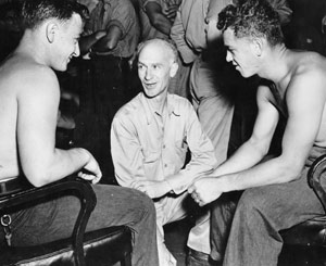 Ernie Pyle kneels speaking to two smiling soldiers.