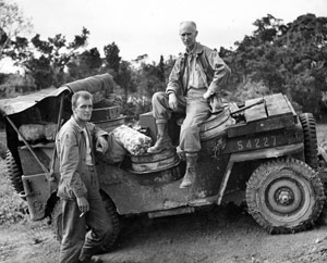Two soldiers pose on a truck.