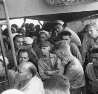 Ernie Pyle stands with a group of soldiers on a boat.