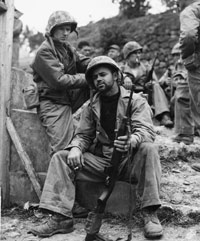 Ernie Pyle sits with a soldier outdoors.