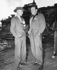 Ernie Pyle stands in a suit outdoors during the war.